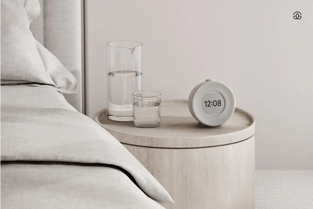A hand reaching for the Mudita Harmony 2 on a nightstand beside a watch, with no phone in the room