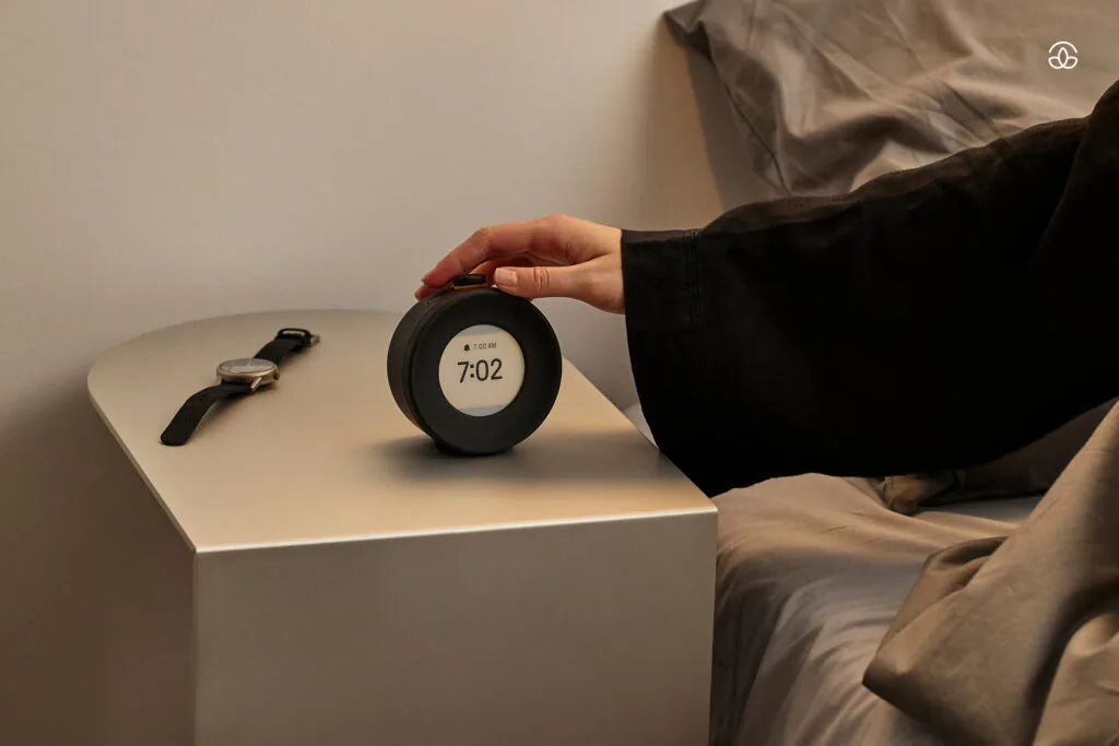 Mudita Harmony 2 on a bedside table beside a bed, E Ink display showing the time